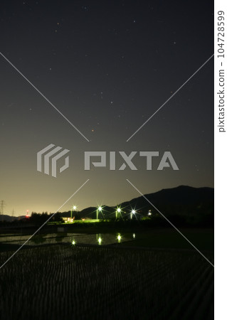 夜幕降臨,北斗市竹川町,舞鶴橋上空升起紅星心宿二。戶外的燈光倒映在稻田裡 夜幕降臨,北斗市竹川町,舞鶴橋上空升起紅星心宿二。戶外的燈光倒映在稻田裡 104728599
