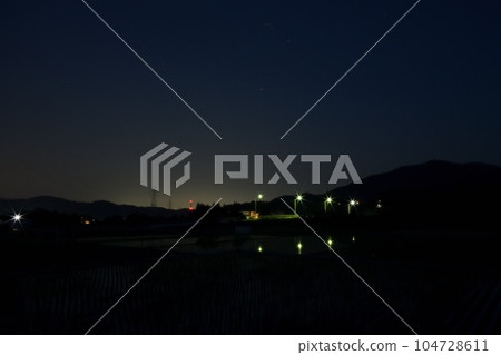 夜幕降臨,北斗市竹川町,舞鶴橋上空升起紅星心宿二。戶外的燈光倒映在稻田裡 夜幕降臨,北斗市竹川町,舞鶴橋上空升起紅星心宿二。戶外的燈光倒映在稻田裡 104728611