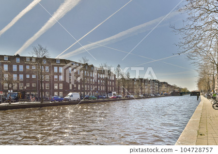some buildings on the side of a body of water with clouds in the sky above them and people walking along it some buildings on the side of a body of water with clouds in the sky above them and people walking along it 104728757
