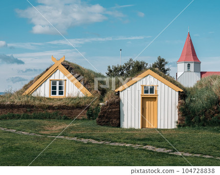 Traditional turf covered house in Glaumbaer, northwestern Iceland. Agricultural fields with horses, and snow-covered mountains in the background 104728838
