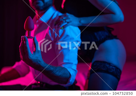 A couple of lovers use an anal plug in the bedroom in neon light. 104732850