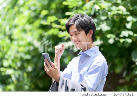 一個年輕人在戶外看著智能手機屏幕,擺出勇敢的姿勢 一個年輕人在戶外看著智能手機屏幕,擺出勇敢的姿勢 104734381