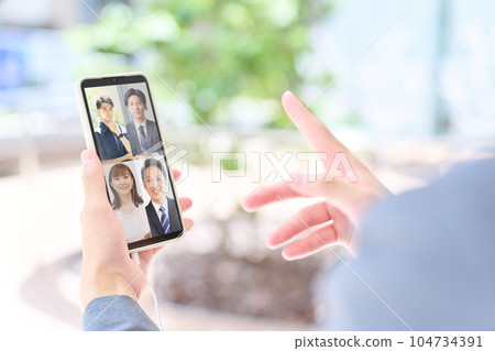 The hand of a business person who is having a video conference on a smartphone The hand of a business person who is having a video conference on a smartphone 104734391