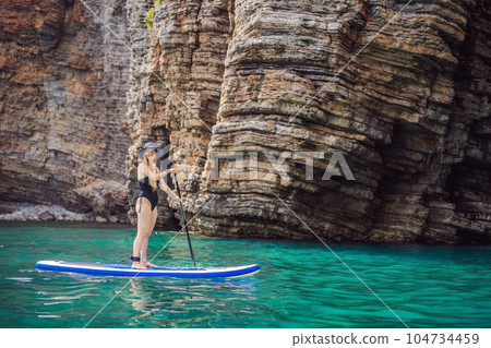 Young women Having Fun Stand Up Paddling in blue water seaamong the rocks in Montenegro. SUP 104734459