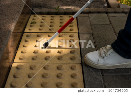 A close-up of a woman's feet with a tactile cane and a tactile tile indicating an obstacle. 104734905
