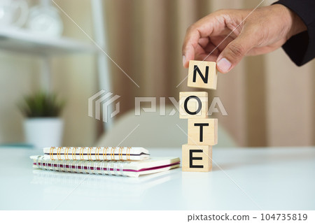 Word NOTE on wood cubes, Hand holding wooden block stacking with note alphabet and notebooks nearby Word NOTE on wood cubes, Hand holding wooden block stacking with note alphabet and notebooks nearby 104735819