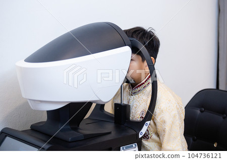 Indian child boy examining eyesight modern ophthalmology equipment in clinic. Indian child boy examining eyesight modern ophthalmology equipment in clinic. 104736121