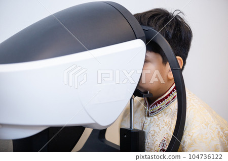 Indian child boy examining eyesight modern ophthalmology equipment in clinic. Indian child boy examining eyesight modern ophthalmology equipment in clinic. 104736122