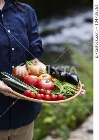 Japanese woman farmer with freshly picked vegetables in front of the river Japanese woman farmer with freshly picked vegetables in front of the river 104738363