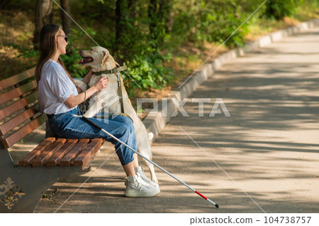 Blind young woman cuddling with guide dog while sitting on a bench. Blind young woman cuddling with guide dog while sitting on a bench. 104738757