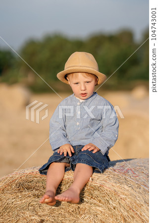 A kid in rural clothes sits on the hay. 104743001