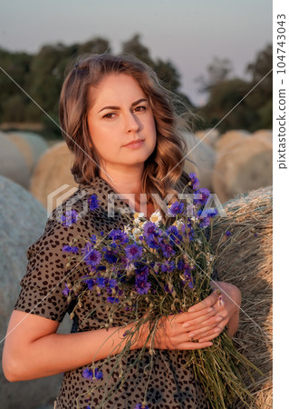 Portrait of attractive young woman in retro dress with a bouquet of wildflowers in countryside. 104743043