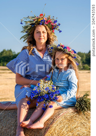 Happy Ukrainian family - mother and daughter in national embroidered clothes stand in field. Support for Ukraine. Happy Ukrainian family - mother and daughter in national embroidered clothes stand in field. Support for Ukraine. 104743593