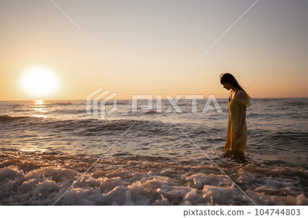 Young woman walks along seashore at sunset. Nature, relax, lifestyle concept. Young woman walks along seashore at sunset. Nature, relax, lifestyle concept. 104744803