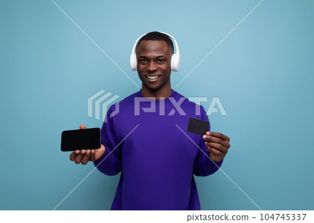 handsome young american man in blue sweatshirt with wireless bluetooth headphones and smartphone on 104745337