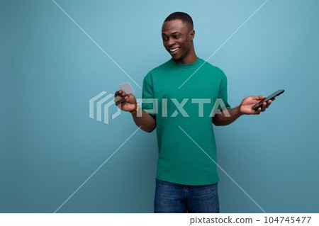 cheerful young american man in t-shirt chatting in smartphone on blue background with copy space 104745477
