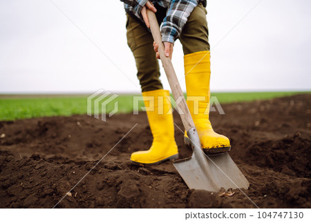 Female Worker digs soil with shovel in the vegetable garden. Agriculture and tough work concept Female Worker digs soil with shovel in the vegetable garden. Agriculture and tough work concept 104747130