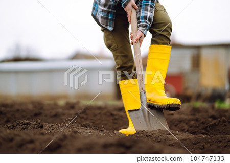 Female Worker digs soil with shovel in the vegetable garden. Agriculture and tough work concept Female Worker digs soil with shovel in the vegetable garden. Agriculture and tough work concept 104747133