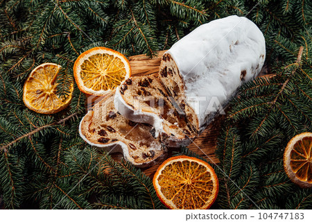 Christmas stollen on wooden background. Traditional christmas german dessert cut into pieces. Cake with nuts, raisins with marzipan and dried fruit on cutting board. baking for xmas 104747183