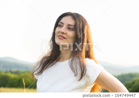 Portrait of a pensive 35-year-old woman in a white T-shirt against the sky in nature in summer. Portrait of a pensive 35-year-old woman in a white T-shirt against the sky in nature in summer. 104749447