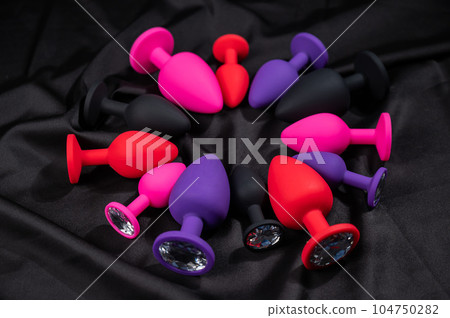 A set of silicone anal plugs in different colors and sizes on a black silk sheet. A set of silicone anal plugs in different colors and sizes on a black silk sheet. 104750282