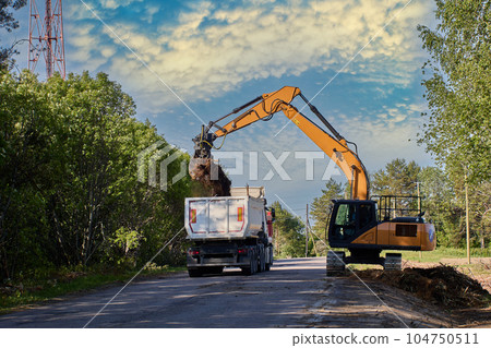 Crawler excavator pours earth into back of dump truck during roadworks to deepen storm drain. Crawler excavator pours earth into back of dump truck during roadworks to deepen storm drain. 104750511