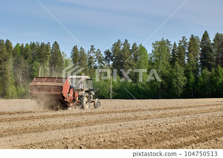 Spring sowing in potato field, potato planter plants potatoes using wheeled tractor. Spring sowing in potato field, potato planter plants potatoes using wheeled tractor. 104750513