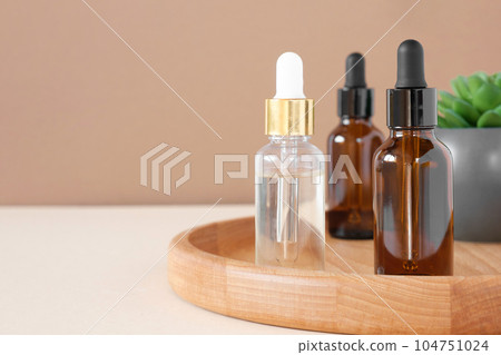 Glass bottles on wooden plate. Natural skin care SPA beauty product design. Mineral organic oil cosmetics on beige background. Earth tones. Mock-Up. Glass bottles on wooden plate. Natural skin care SPA beauty product design. Mineral organic oil cosmetics on beige background. Earth tones. Mock-Up. 104751024