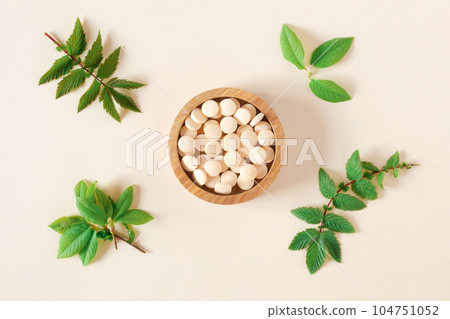 Directly Above Shot Of Pills and green leaves. Tablets in wooden bowl on beige neutral colors background. Homeopathic medicine. Organic medical capsules with herbal plant. Table top view. Copy space 104751052