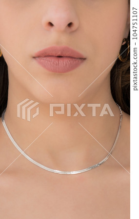 Young woman wearing golden earrings and a silver snake chain necklace. Young woman wearing golden earrings and a silver snake chain necklace. 104751107