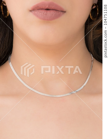 Young woman wearing golden earrings and a silver snake chain necklace. Young woman wearing golden earrings and a silver snake chain necklace. 104751108
