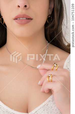Young woman wearing golden earrings, interlocked rings and a silver snake chain necklace. Young woman wearing golden earrings, interlocked rings and a silver snake chain necklace. 104751109