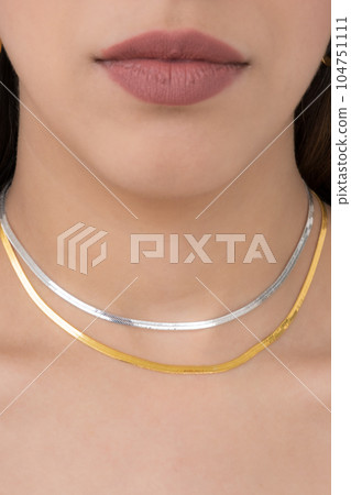 Young woman wearing golden earrings and a golden and a silver snake chain necklace. Young woman wearing golden earrings and a golden and a silver snake chain necklace. 104751111