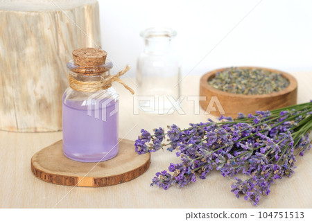Dry lavender flowers in wooden bowl and bottle of essential lavender oil or infused water on white background. Natural organic ingredients for herbal cosmetics. Spa massage set, lavender product Dry lavender flowers in wooden bowl and bottle of essential lavender oil or infused water on white background. Natural organic ingredients for herbal cosmetics. Spa massage set, lavender product 104751513