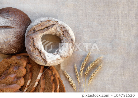 Baked bread. Loaf of Bread. Fresh Bakery Products on Wooden Board. Healthy Food Concept. Top View. Flat lay. Slices of Homemade Sourdough Bread with Flour on Rustic Linen Background. Wheat Spikes 104751520