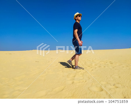Young man in straw hat and dark shorts walking in desert Young man in straw hat and dark shorts walking in desert 104751859