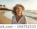 Happy retired woman wearing shawl sitting relaxed on sand at the beach. Senior caucasian woman sitting on the beach outdoors 104752515