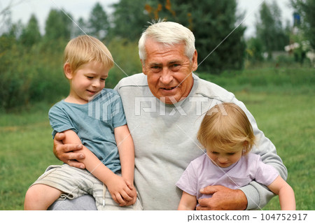 Grandfather and grandchildren have fun during walk In Park. Happy family time. Old man grandpa hugging children boy and girl. Summer day. Smiling Senior male spending time with his grandkids together 104752917