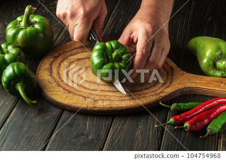 The cook cuts fresh green peppers to prepare a delicious salad at home. Peasant food. The cook cuts fresh green peppers to prepare a delicious salad at home. Peasant food. 104754968