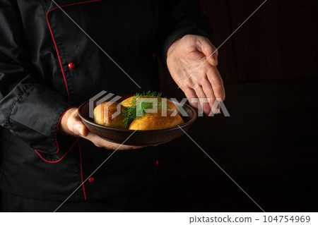 The chef presents in his hand a plate of freshly baked buns or dill pies. Free black space for menu or recipe 104754969