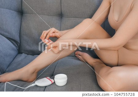 Woman is applying cream on leg after using electric epilator, body closeup. Woman is applying cream on leg after using electric epilator, body closeup. 104755728