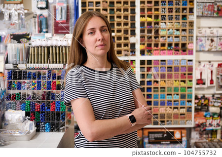 Confident young woman, sales manager, seller looking at camera, standing with her arms folded in school stationery shop 104755732