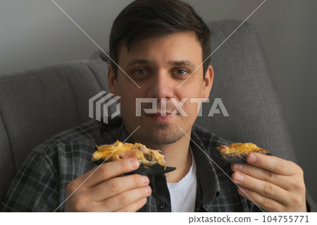 Young man bachelor sitting on sofa at home and eating two slices of tasty pizza. 104755771