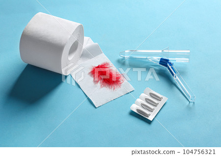 Anoscope, suppositories and toilet paper with red feather on light blue background. Hemorrhoid treatment 104756321
