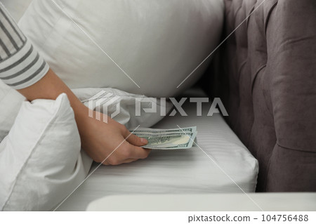 Woman hiding dollar banknotes under pillow in bedroom, closeup. Money savings Woman hiding dollar banknotes under pillow in bedroom, closeup. Money savings 104756488