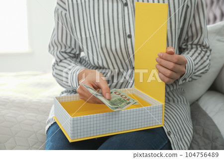 Woman hiding dollar banknotes in box at home, closeup. Money savings 104756489