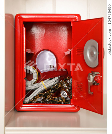 Open red steel safe with money and jewelry on shelf 104756490