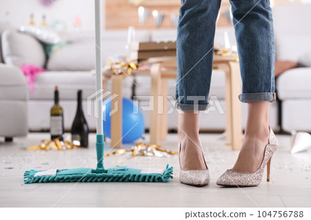 Young woman with mop cleaning messy room after party, closeup of legs 104756788