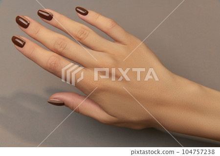 Beautiful groomed womans hand with trendy autumn nail design on brown background 104757238