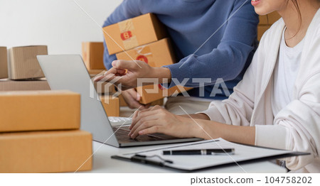 Happy couple people packing parcel boxes, couple lover checking order online on laptop at home 104758202